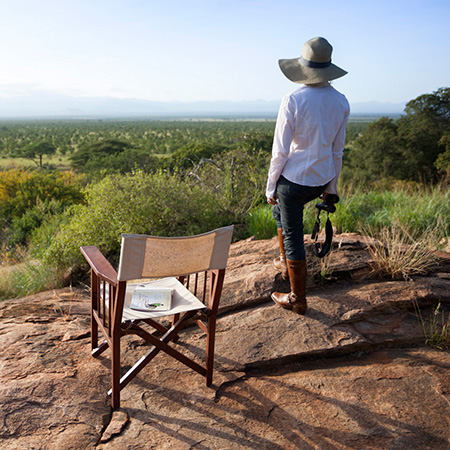 A woman on safari looks out over Meru National Park from a rock kopje in Kenya.