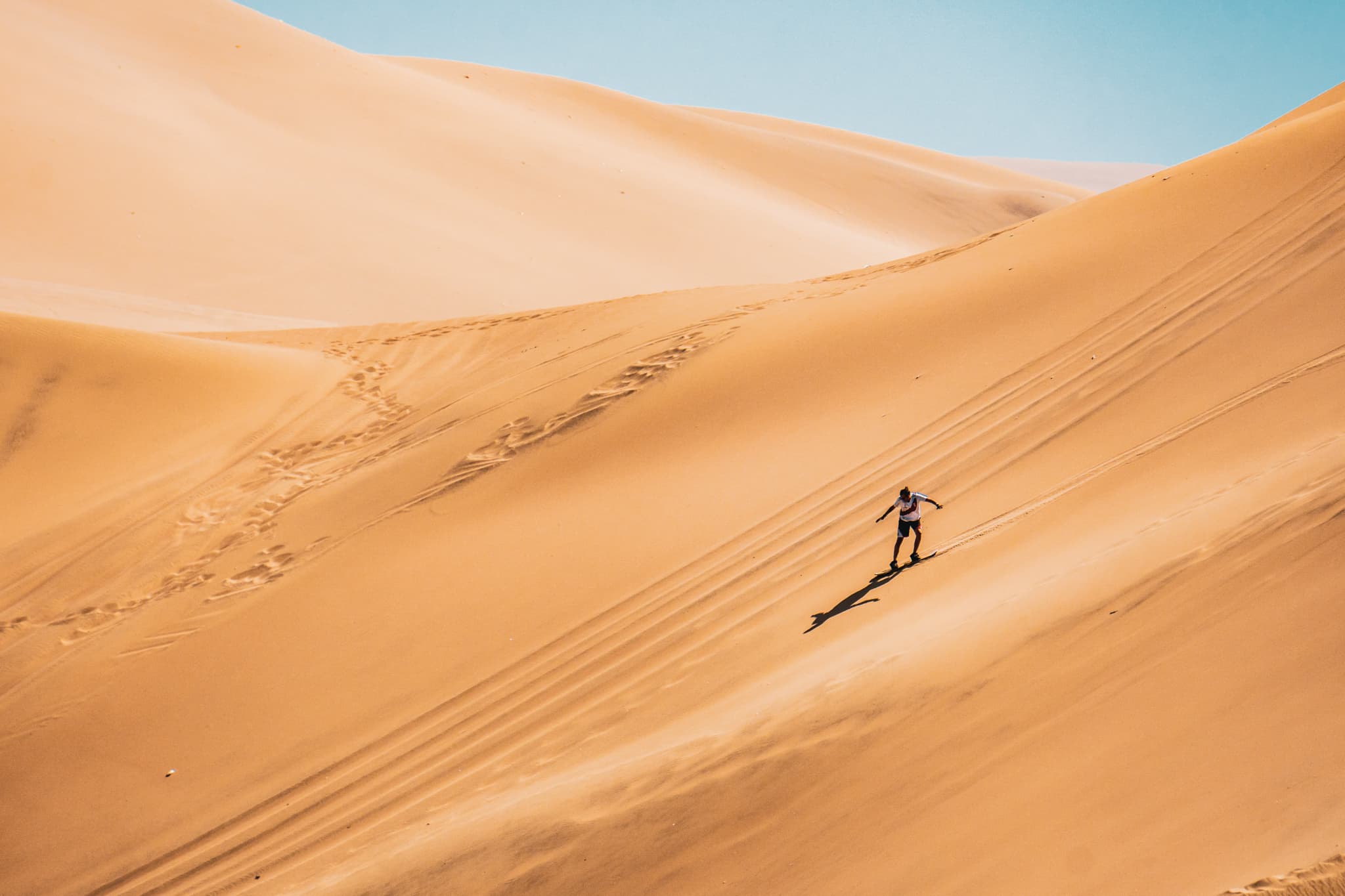 Adventurer sandboarding down golden desert dunes under clear skies—an epic experience with premier access expeditions.