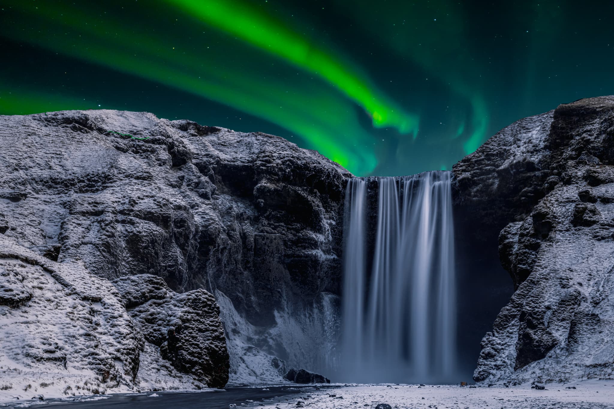 Skogafoss waterfall in the winter at night under the northern lights, Iceland