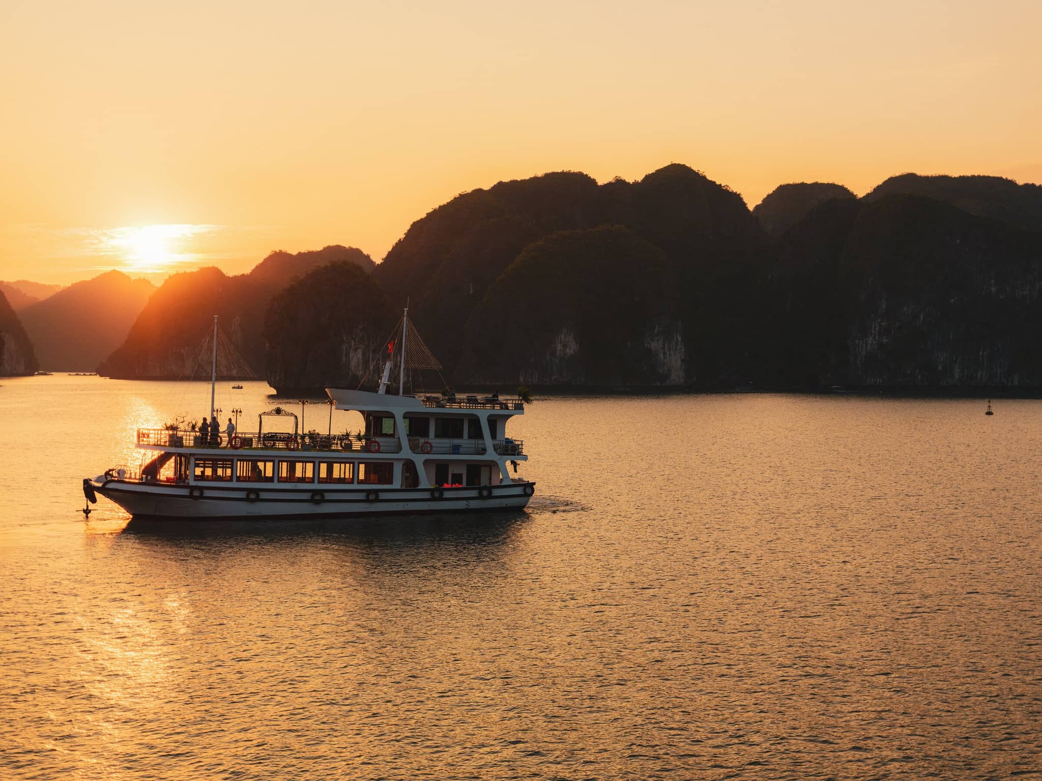 Luxury cruise boat sailing at sunset in scenic bay with limestone cliffs and golden reflections on the water.