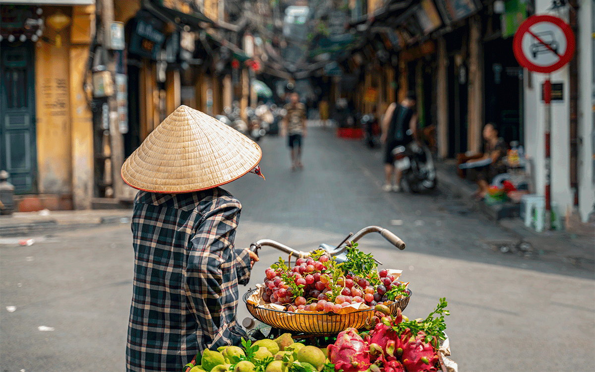 A street vendor with bike loaded of tropical fruits in old town street in Hanoi
