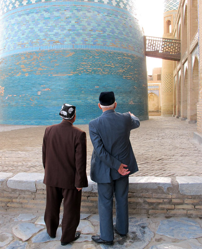Two men stand in front of the turquoise Kalta Minor Minaret in Khiva, Uzbekistan, on the Silk Road