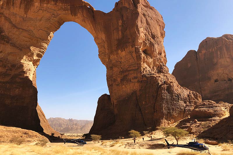 Helicopter at the base of a natural arch formation in Chad's Ennedi Plateau