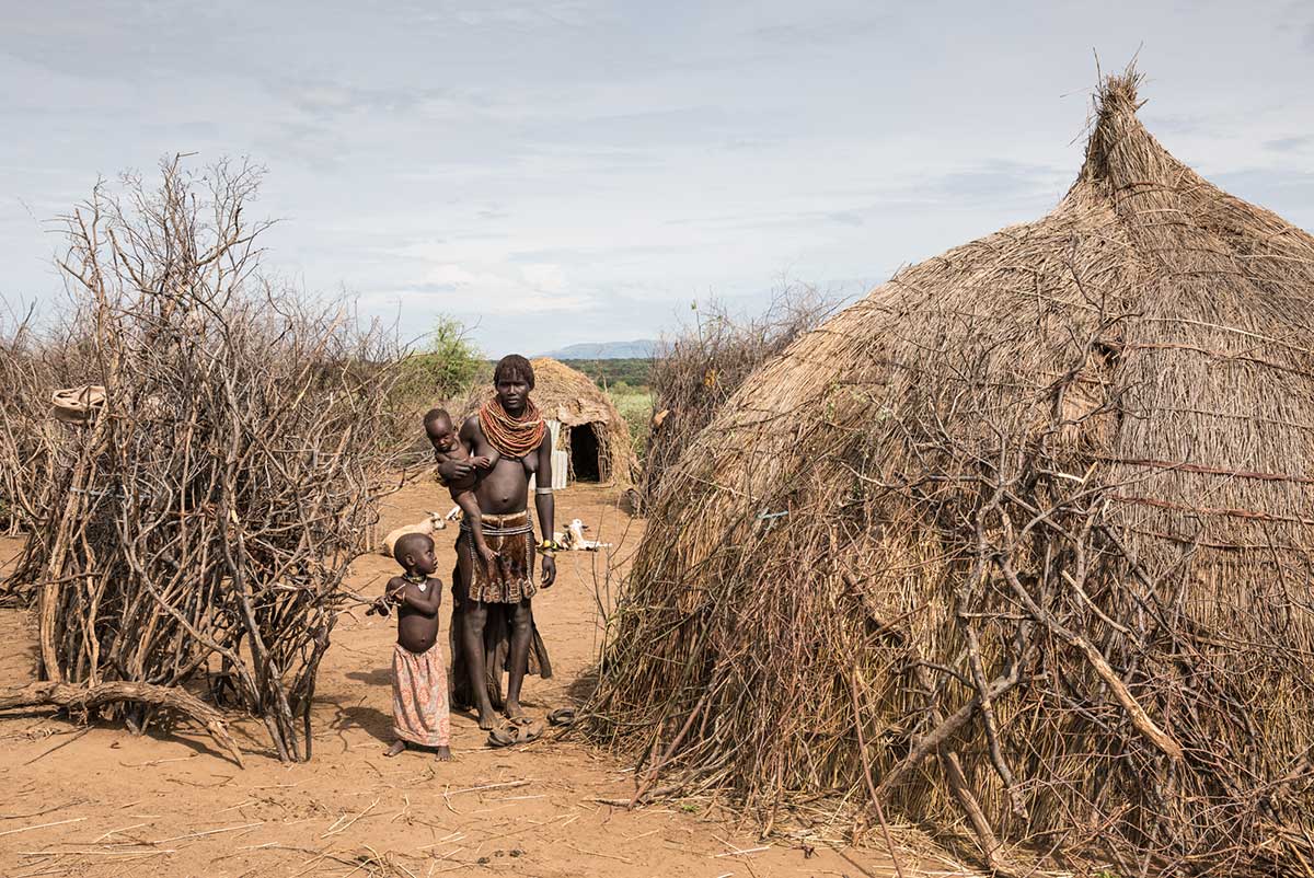 Nyangatom woman and children standing among their woven twig huts.