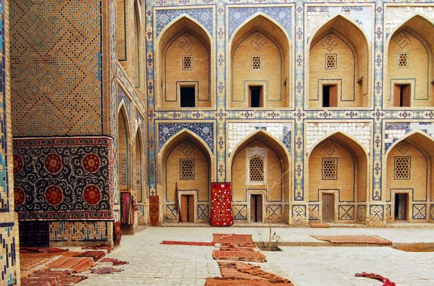 Uzbekistan, Bukhara, arched entrance in a row of historic buildings with carpets lying on courtyard.