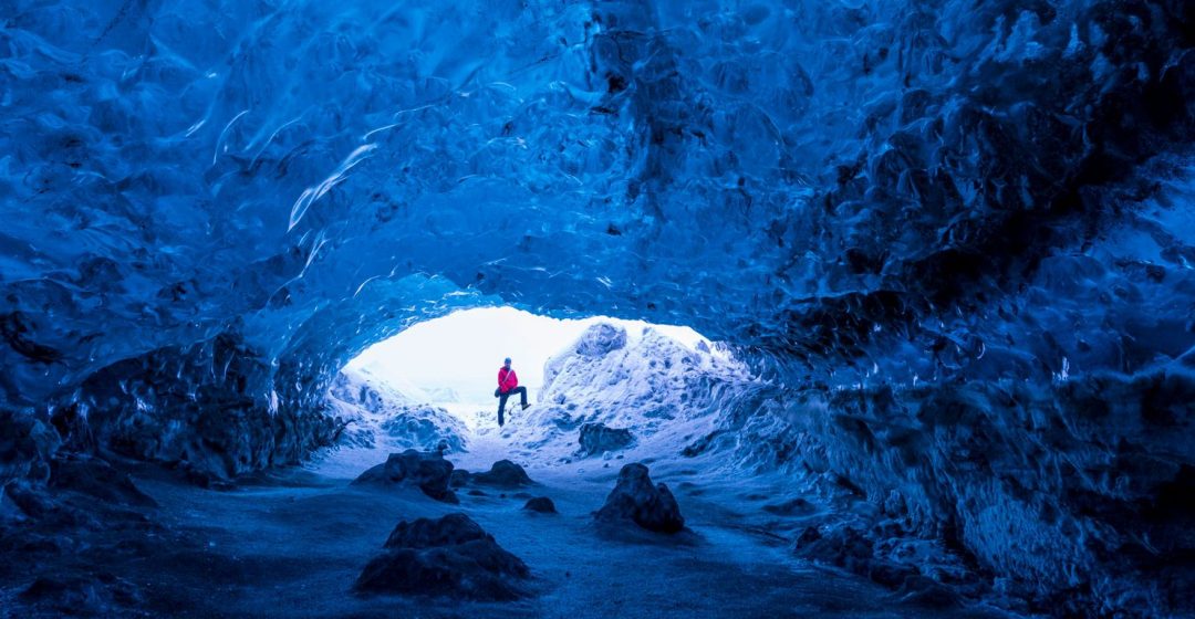 Man standing at entrance to an ice cave beneath a glacier, Iceland