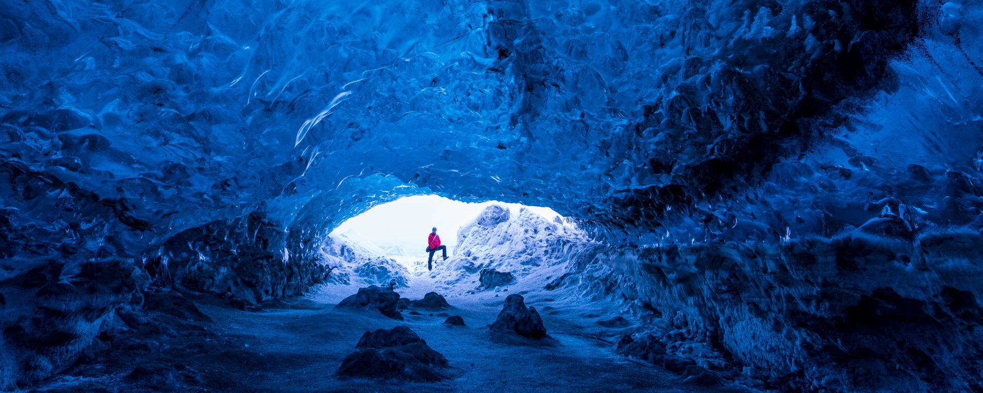 Man standing at entrance to an ice cave beneath a glacier, Iceland