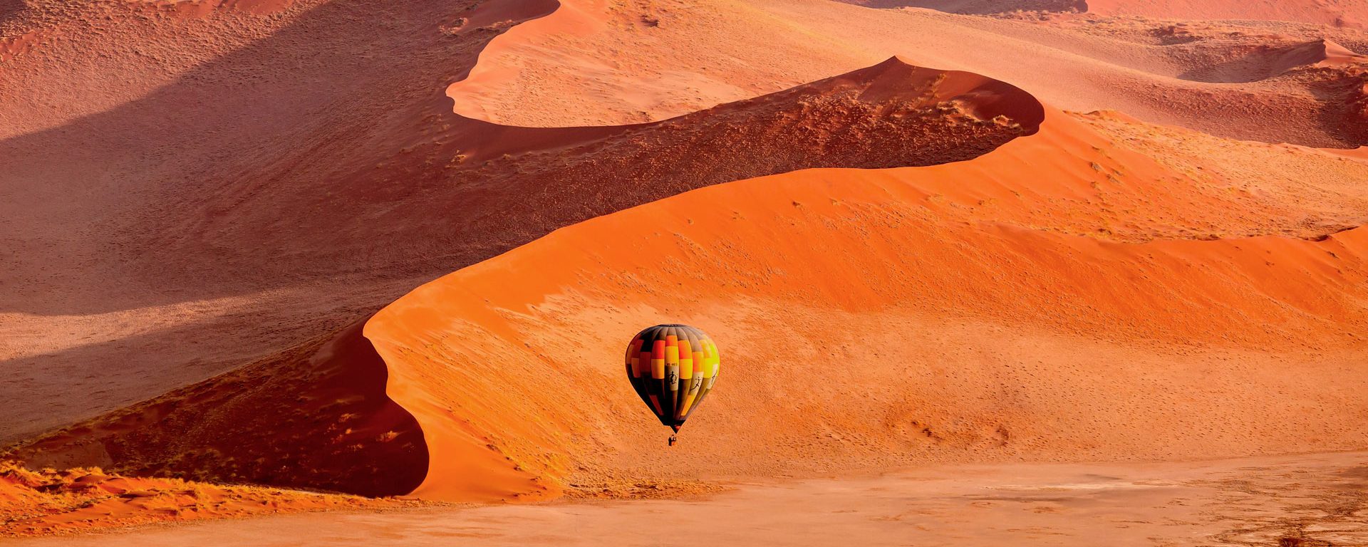 A hot air balloon floats across dunes in Namibia