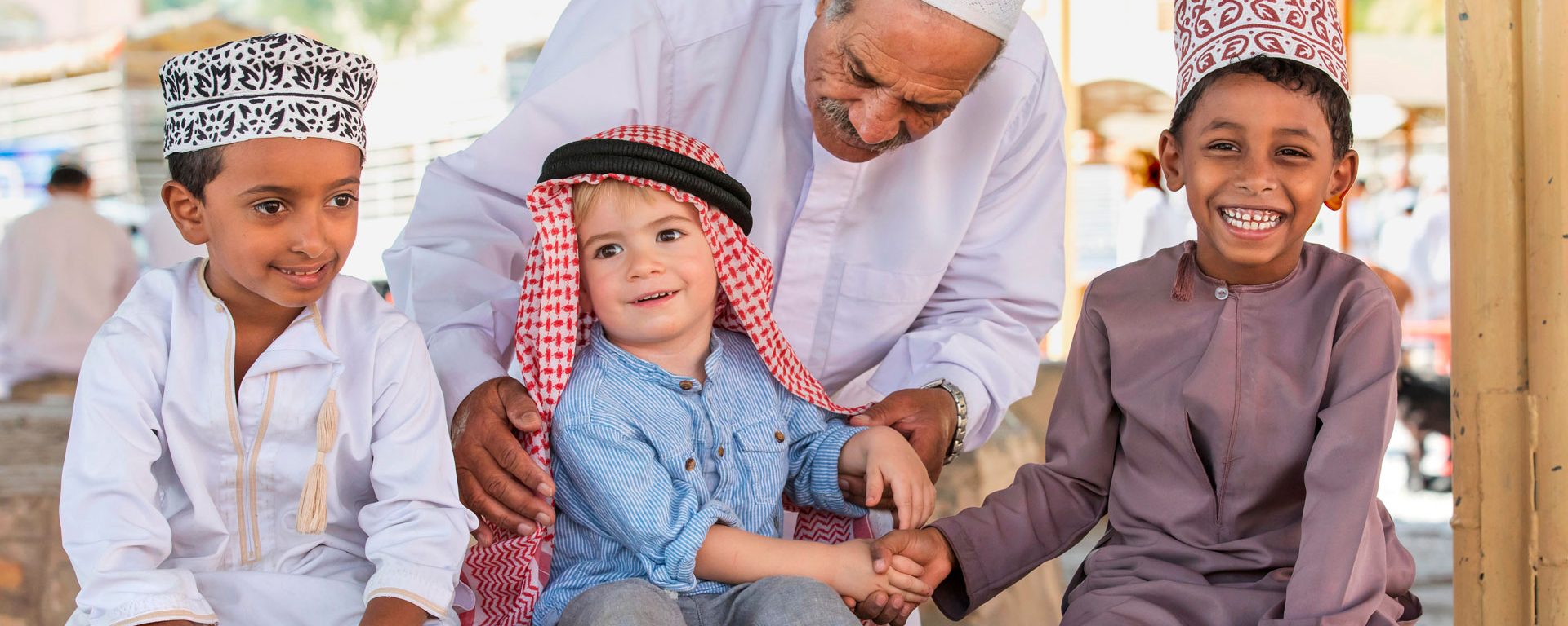 An Omani man helps a young European child shake hands with Omani children, Nizwa, Oman