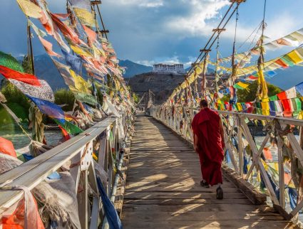 A monk walks across a bridge covered in prayer flags in Leh, in the Ladakh region of India