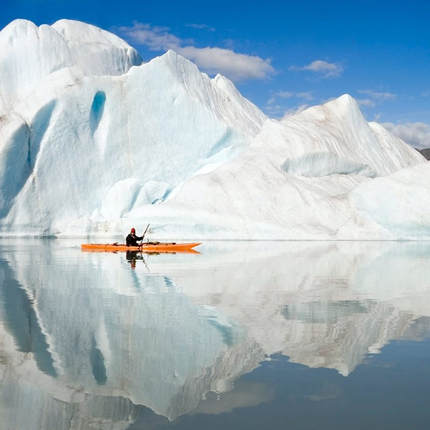 A kayaker paddles past an iceberg in the fjords of Alaska