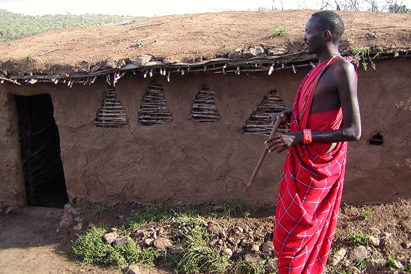 Maasai man in front of thatched roof hut, Kenya