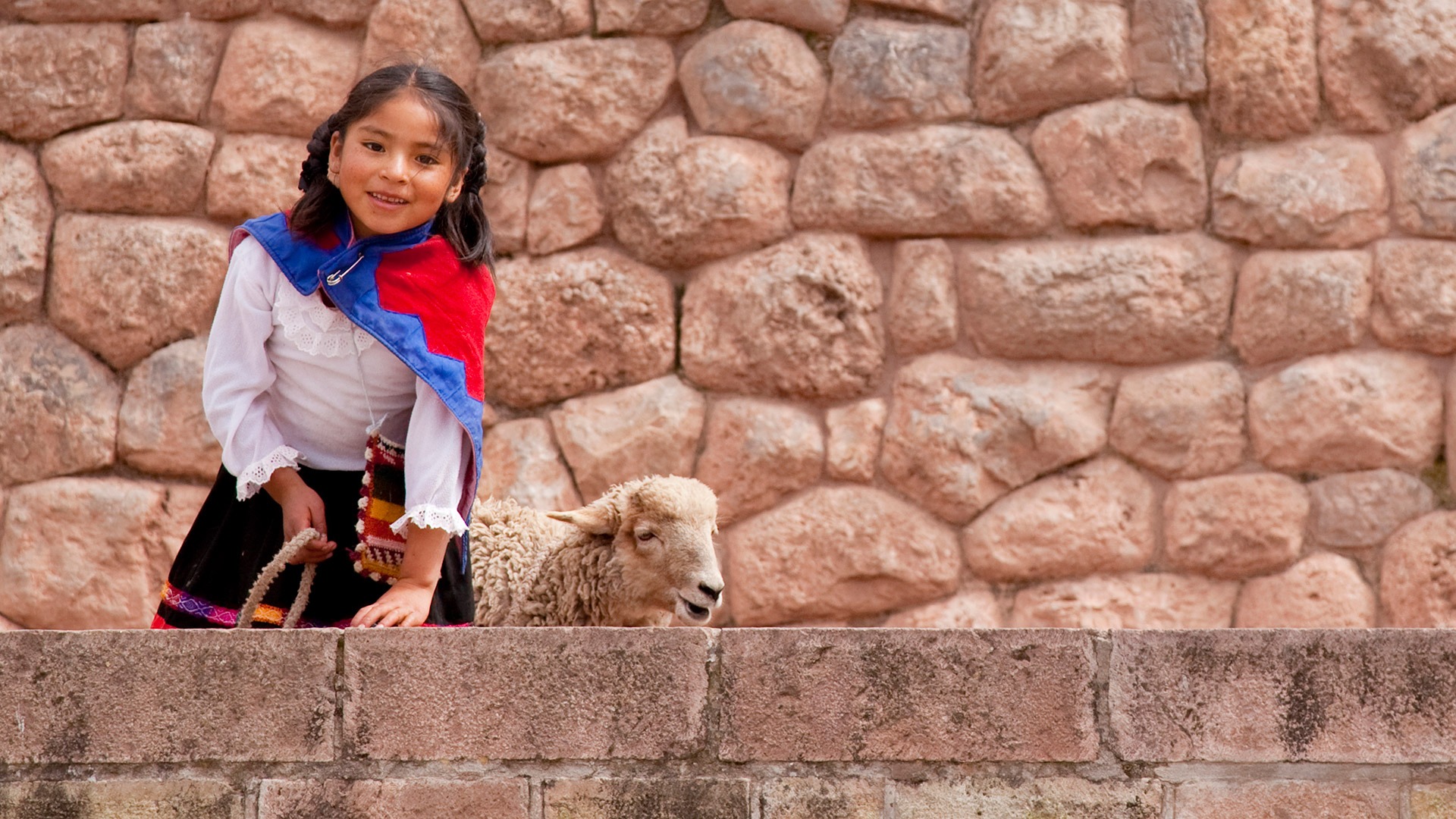 Girl and her sheep in front of a stone wall in Cusco, Peru