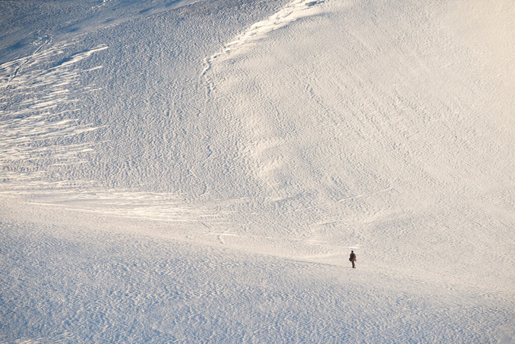 Snowshoer seen as a speck against a wall of ice in Antarctica